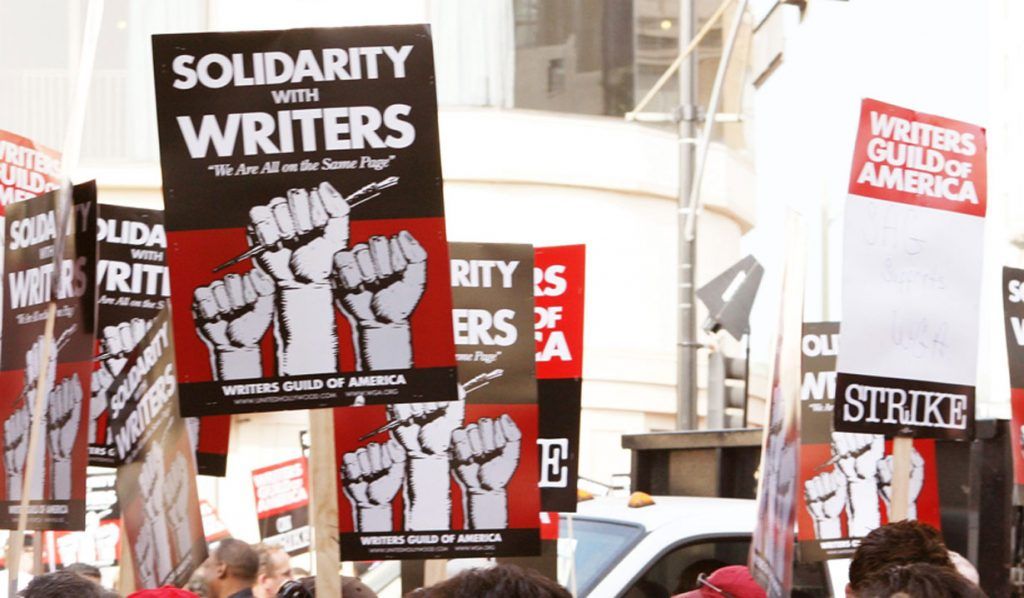 The image is of picket signs in the air supporting the Writers Guild of America strike.